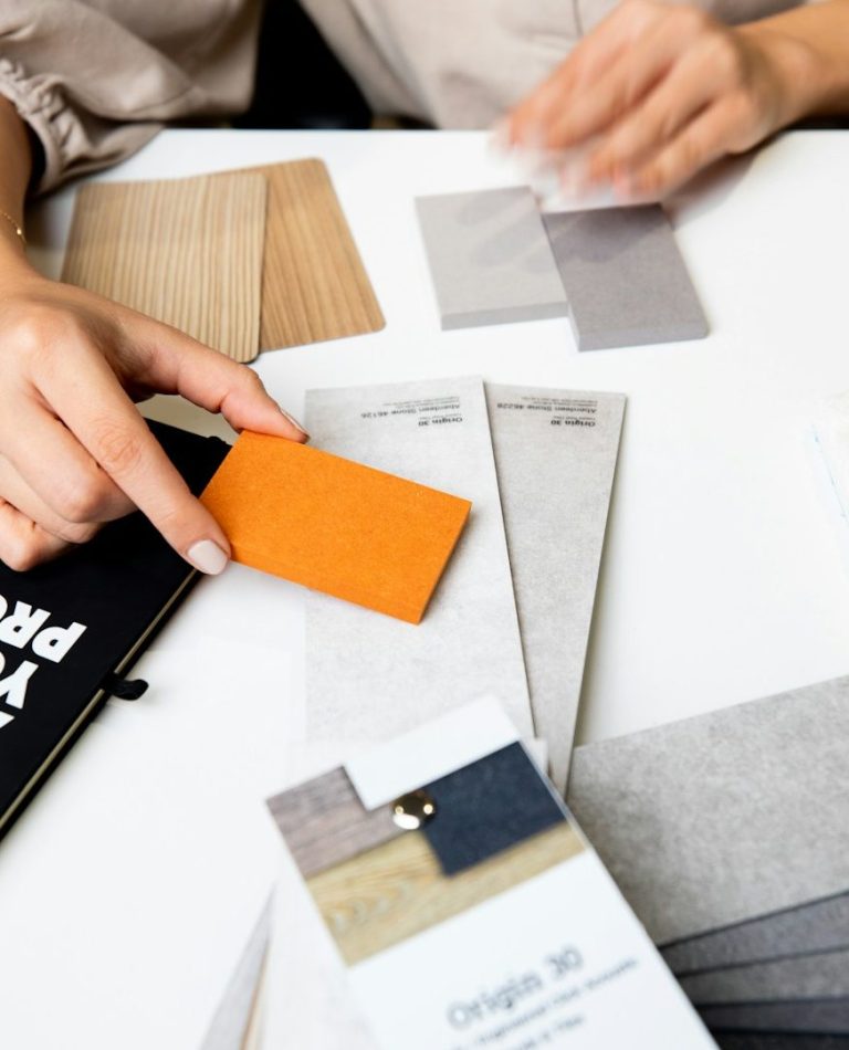 Hände halten Farbmuster und Layoutkarten auf einem Tisch.
