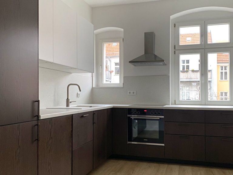 Moderne Küche mit dunklen Holzschränken und hellem Arbeitsbereich. Fenster für Tageslicht in einer Altbauwohnung in Berlin. 